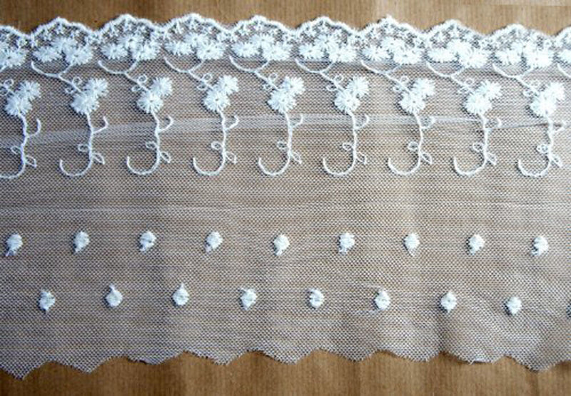 Embroidered tulle lace border in white on a roll