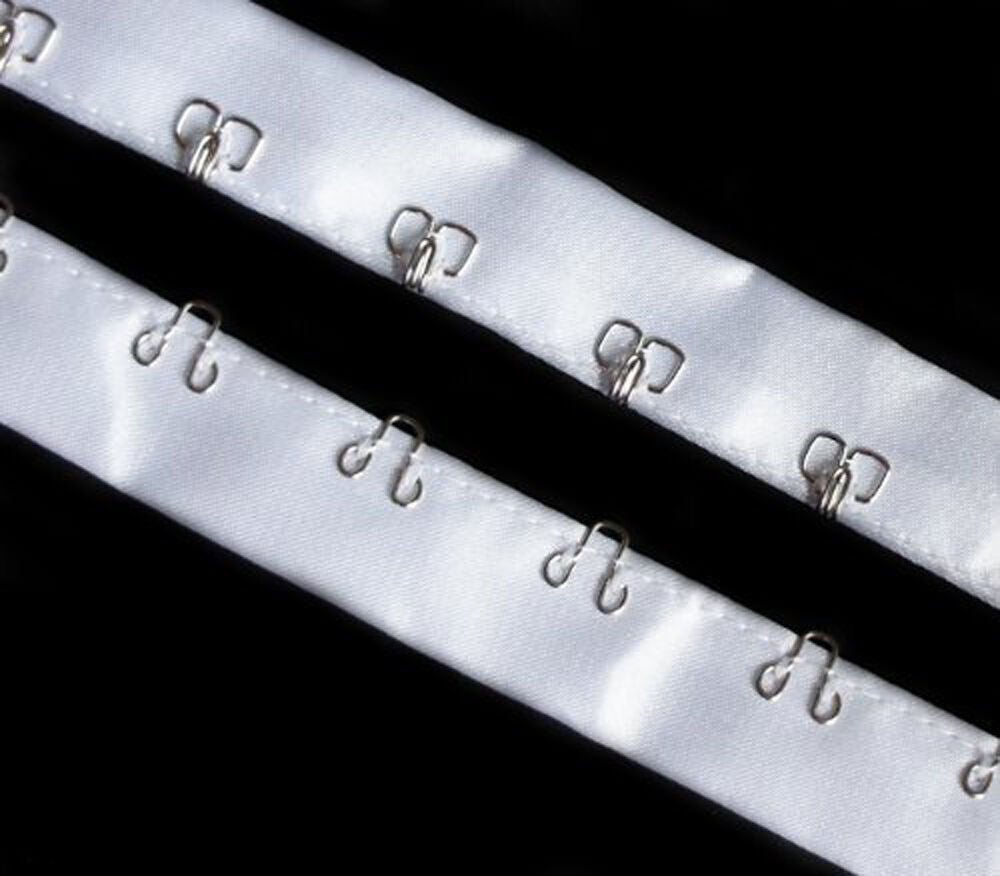 Close-up of silver hook and eyes on white satin ribbon tape.