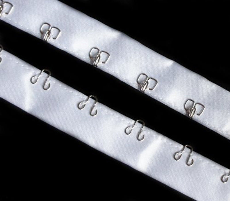 Close-up of silver hook and eyes on white satin ribbon tape.