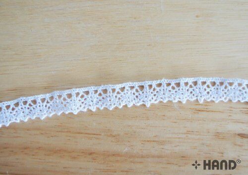 Roll of white cotton lace trim displayed on a craft table.