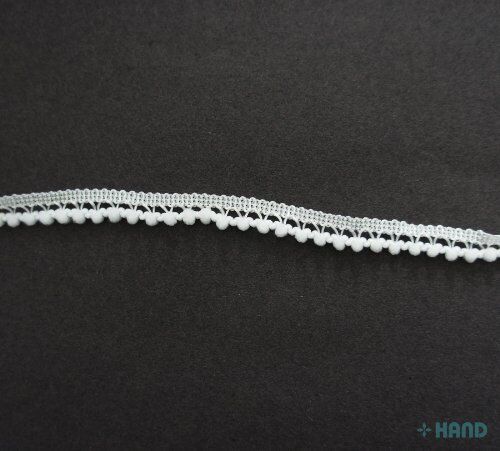 Tiny white pom pom trim displayed with sewing tools and fabric