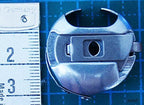 Towa bobbin case placed next to a sewing machine