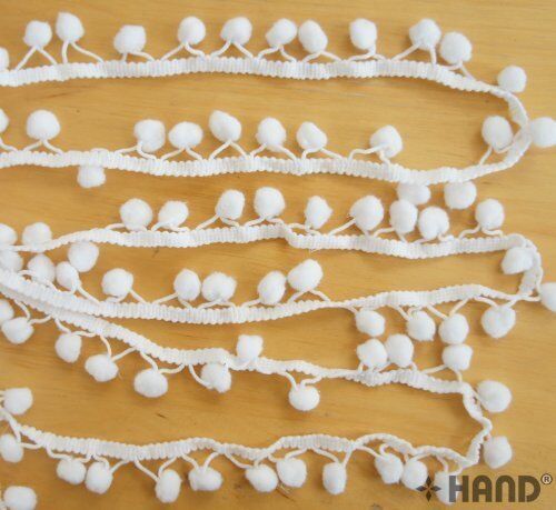 Mini white pom pom fringe displayed on a crafting table.