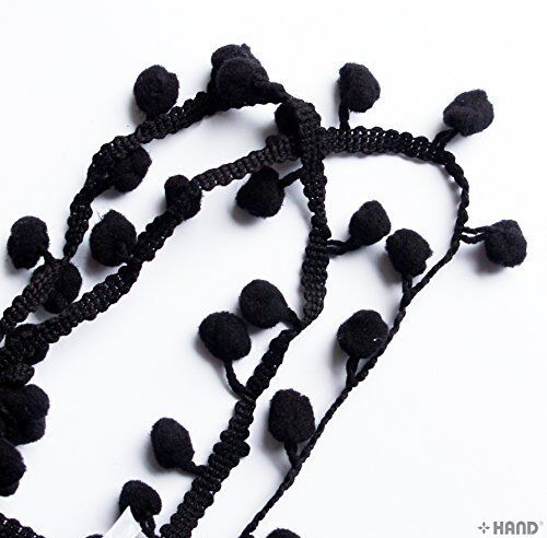 Mini black pom pom fringe displayed on a sewing table with tools.