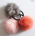 Three assorted colours of pom pom hair bands displayed together.