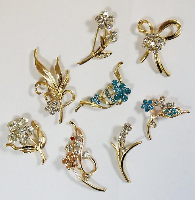 Assorted designs of gold tone gemstone flower brooches on a neutral background.