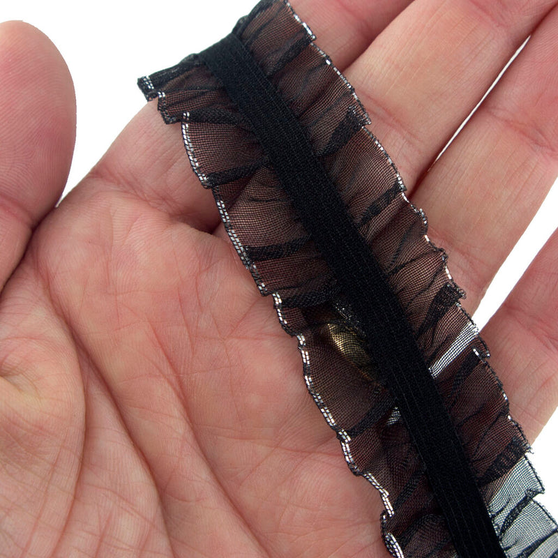 Black elasticated ruffle trim with silver edging on a spool.