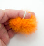 Close-up of orange decorative fluffy pom pom trims with small rubber bands.