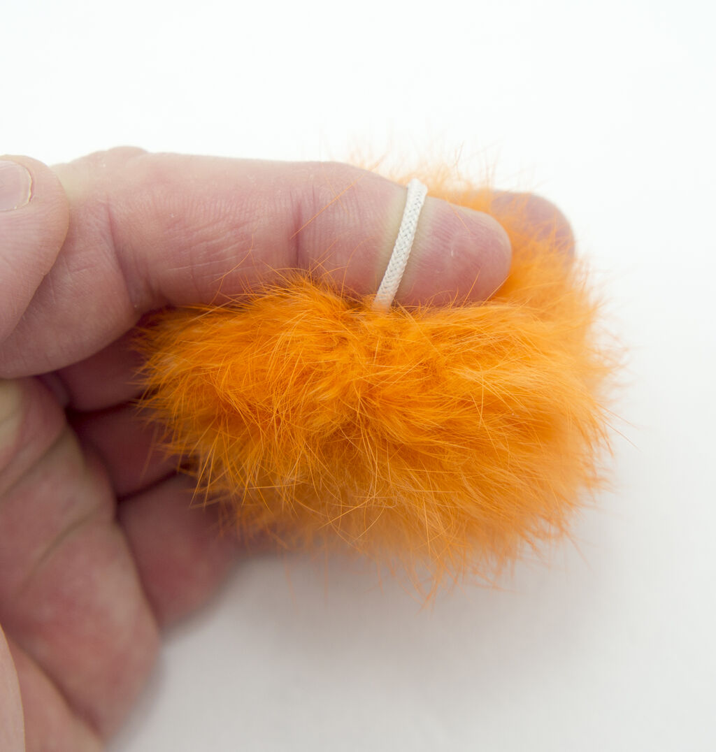 Close-up of orange decorative fluffy pom pom trims with small rubber bands.