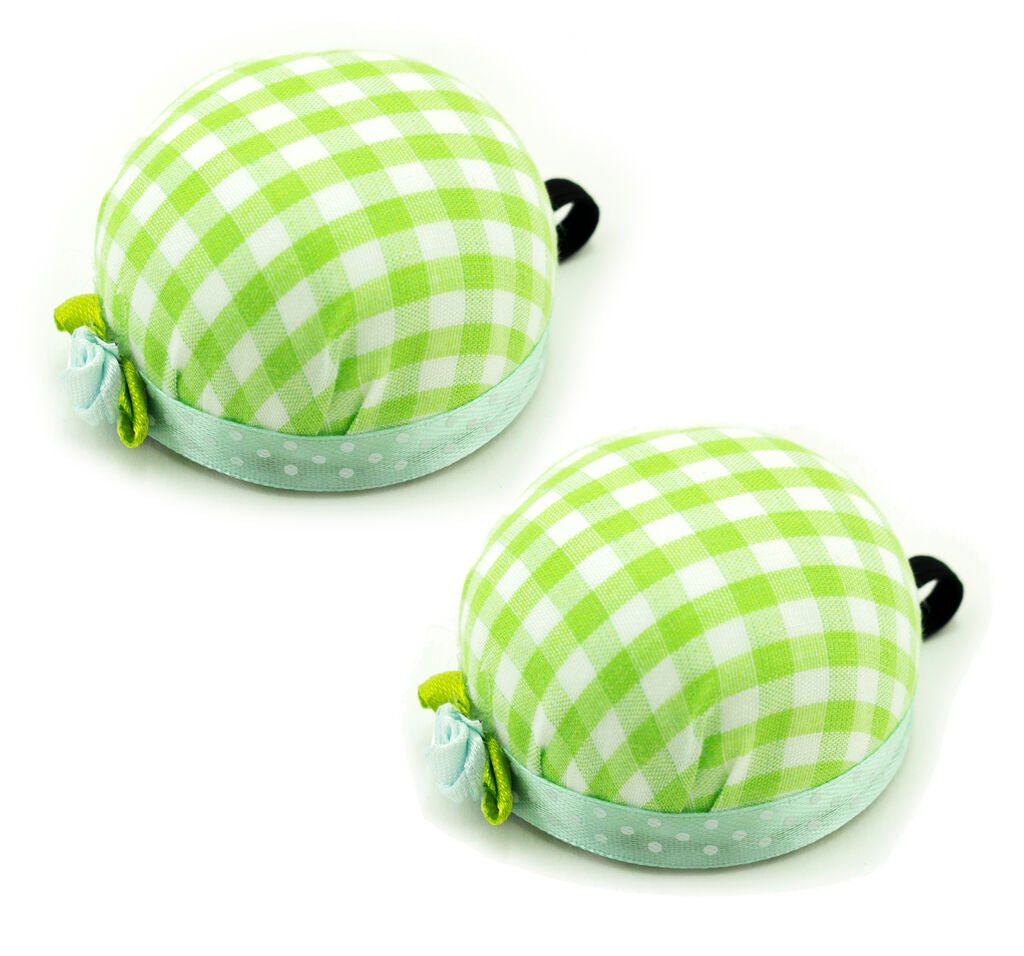 Green check wrist pin cushion on a sewing table with pins.