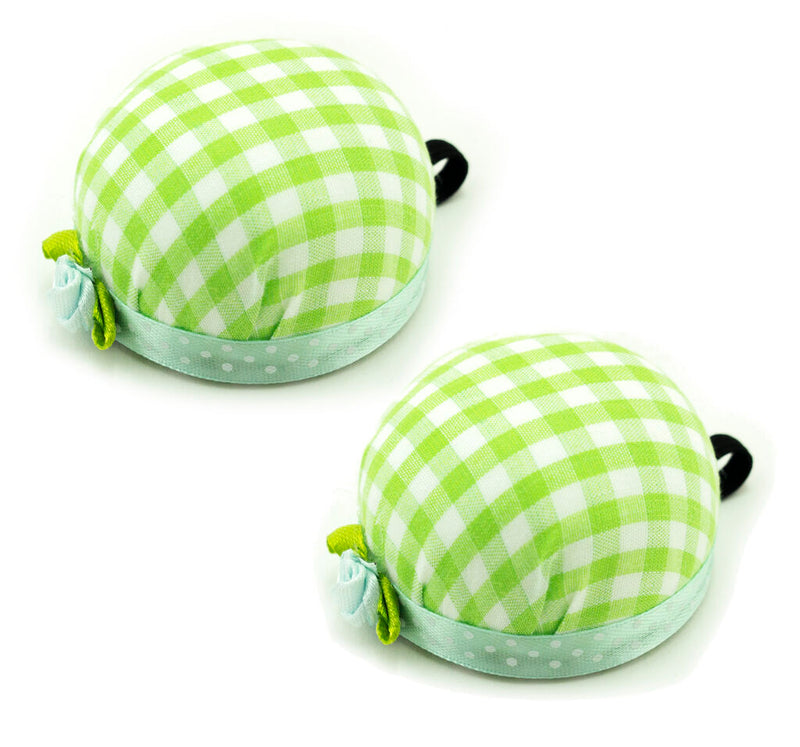 Green check wrist pin cushion on a sewing table with pins.
