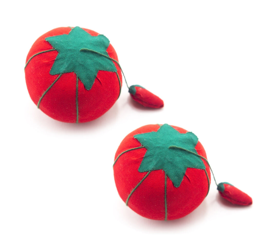Two small tomato pin cushions, 50 mm diameter, on a sewing table.