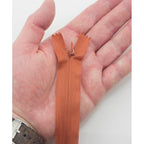 Close-up of a cinnamon brown invisible zipper with metal zip head.