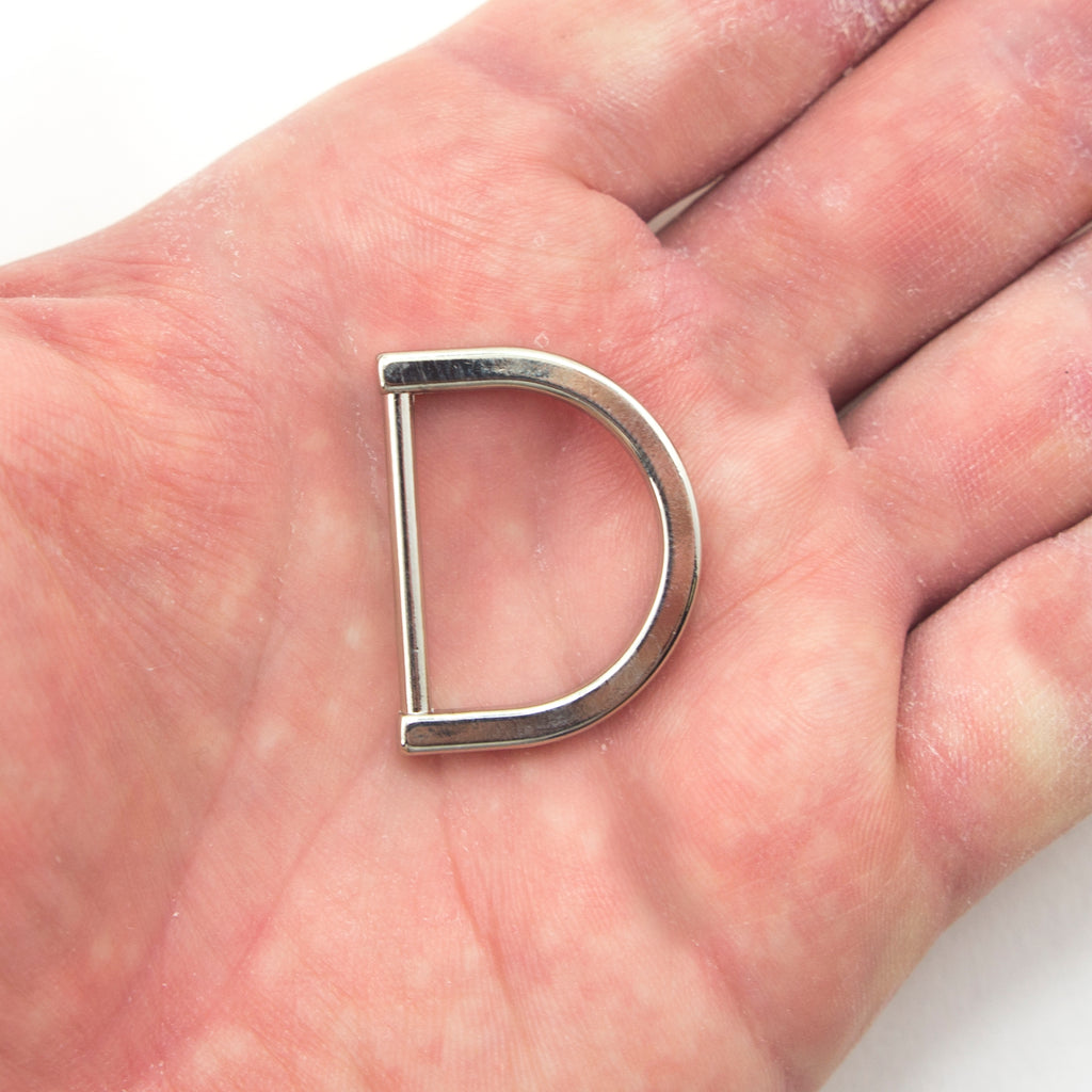 Close-up of a silver tone D ring showing its size and finish.