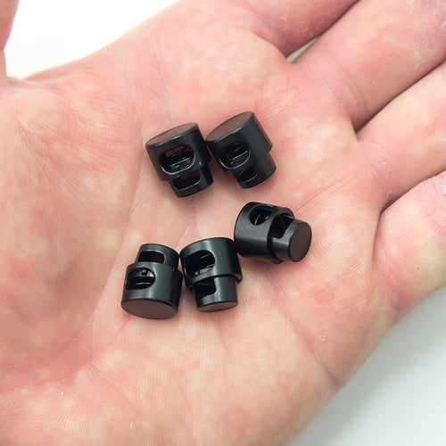 Close-up of a black metal spring stop cord toggle lock showing oval hole size.