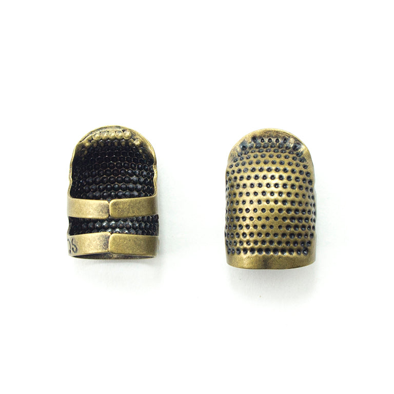 Two antique bronze tone brass thimbles on a white background.