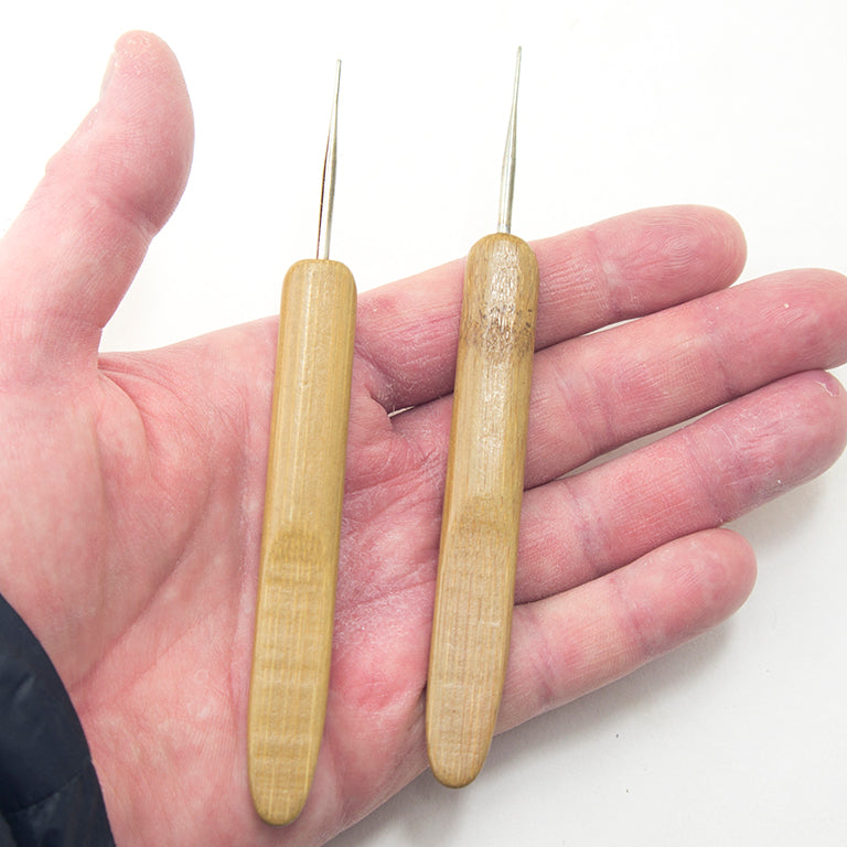 A hand holding a bamboo crochet hook for crafting.
