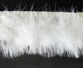 Close-up of white goose feather fringe trim on a roll.